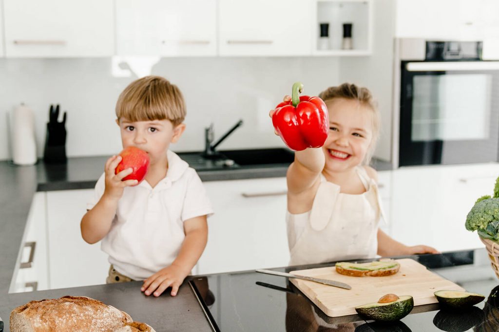 zwei Kinder in der Küche essen Gemüse