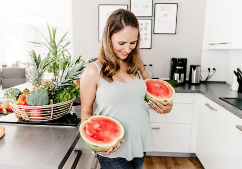 Foto von veganer Schwangeren mit Wassermelonen und Babybauch